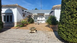 A courtyard with a paved walkway, a central seating area with chairs and a table, and a white building with a tiled roof. - House in Banyeres de Mariola (Banyeres de Mariola)