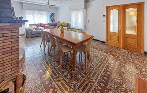 Un comedor con una mesa y sillas de madera, un tapete estampado y una pared de ladrillo.