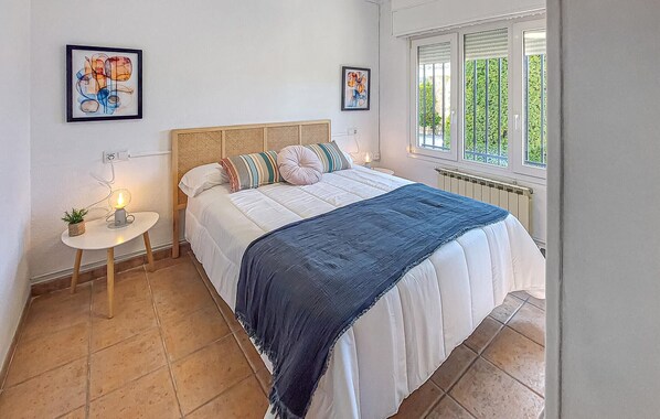 Un dormitorio con cama, una mesita de noche con lámpara, dos obras de arte enmarcadas y una ventana con vistas a zonas verdes.
