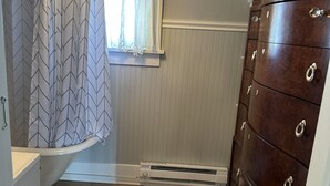 A bathroom with a shower curtain, a window, a wooden dresser, and a radiator. - Broadmoor Guest Mother-in-Law Suite (Colorado Springs)