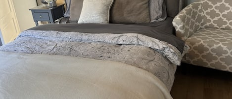 Un dormitorio con cama, mesita de noche, lámpara y alfombra estampada.