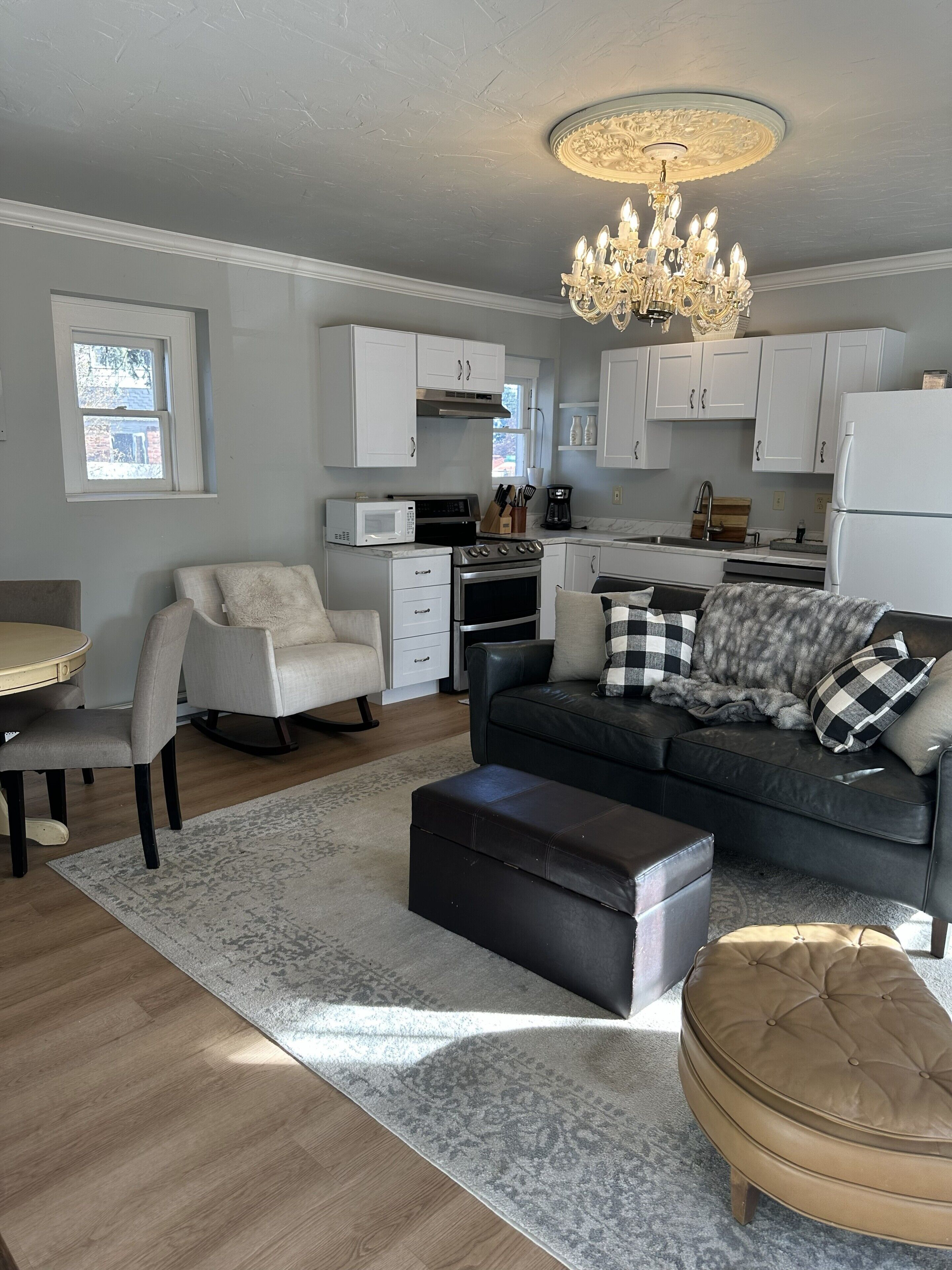 A modern living room with a sofa, ottoman, and a dining area with a table and chairs.
