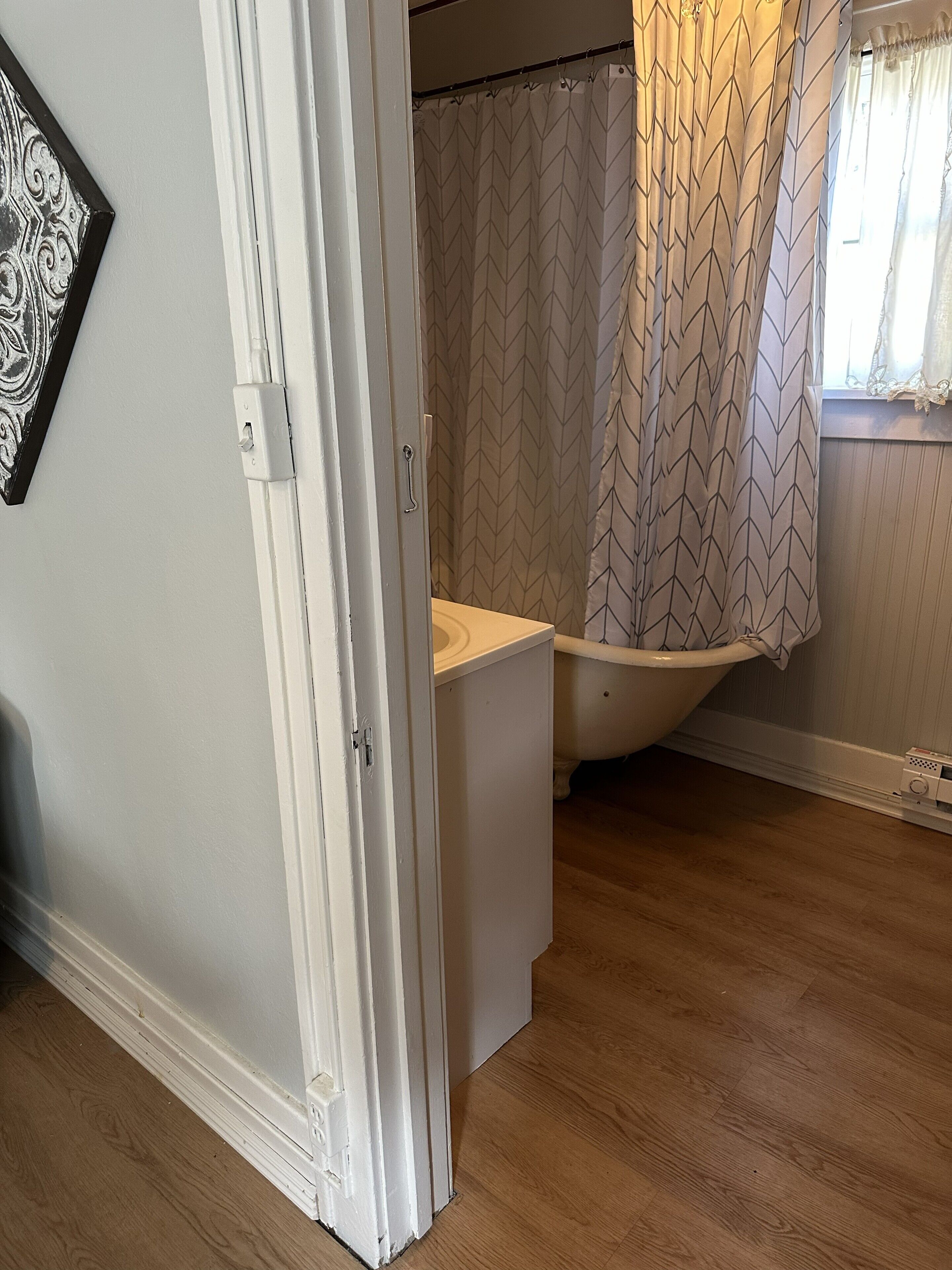 A bathroom with a white bathtub, a shower curtain with a geometric pattern, and a wooden floor.