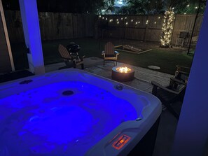 Un bain à remous doté d’un panneau de commande, entouré d’un espace de détente extérieur et d’un foyer.