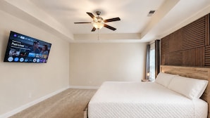 Quarto com cama, ventilador de teto, televisão na parede e janela com persianas.