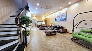 A spacious living area with a herringbone floor pattern, a staircase with a wooden railing, a dining area with a table and chairs, and a hanging chair with green cushions. - Ha Anh Villa Ninh Binh (Hoa Lu)