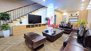 A modern living room with a staircase, a flat-screen TV, leather sofas, a coffee table, and potted plants. - Ha Anh Villa Ninh Binh (Hoa Lu)