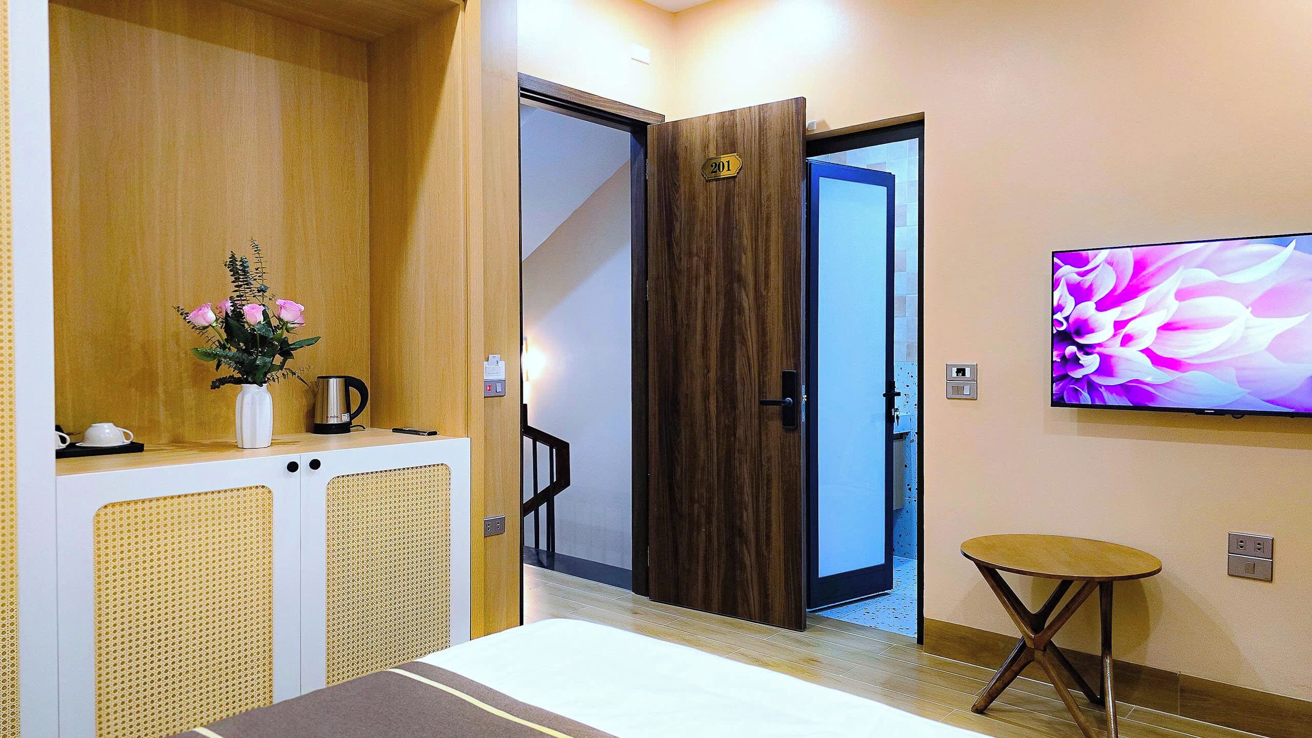 A hotel room with a bed, a small table, a TV on the wall, and a door leading to another room.
