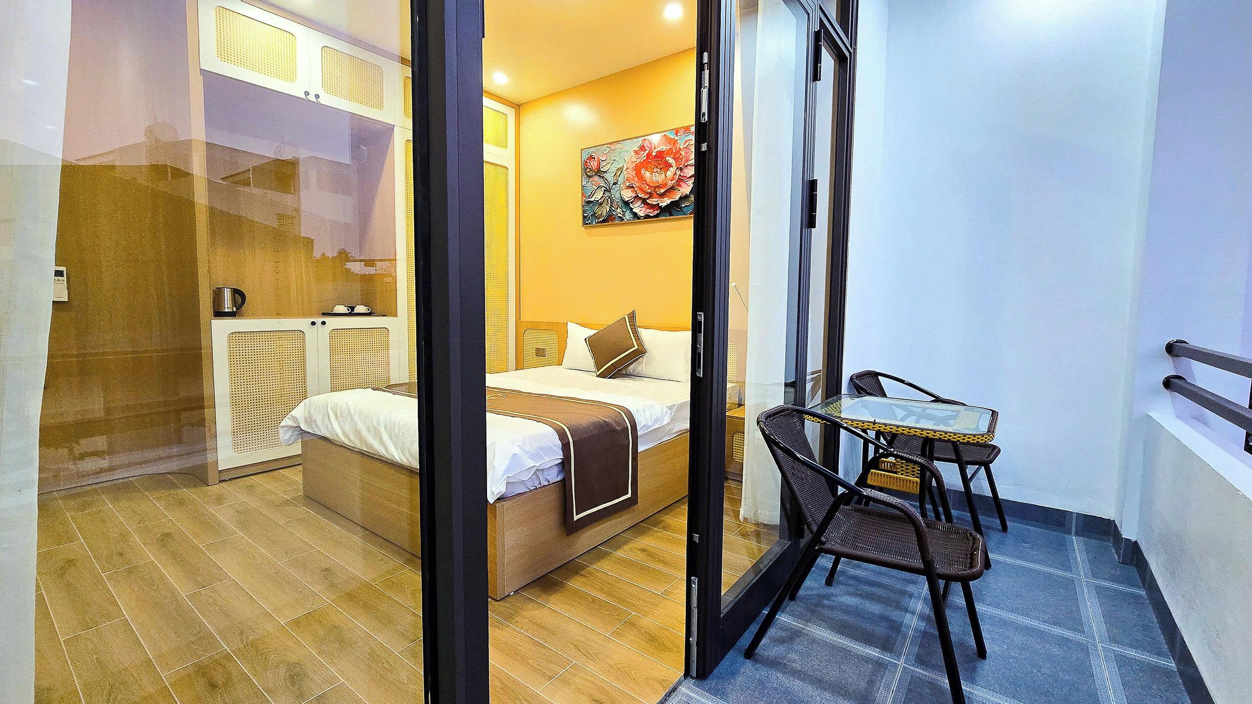 A hotel room with a bed, a small table, and a chair. There is a painting on the wall and a window with a view.