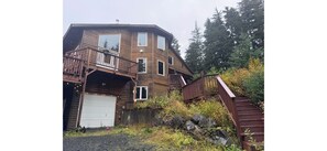 A multi-level wooden cabin with a garage, deck, and staircase leading to a second level. - Hilltop Hideaway~ Seclusion in the Last Frontier (Seward)