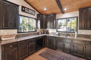 A kitchen with dark wood cabinets, granite countertops, and a window with a view of the outdoors. - Private hot tub, Gorgeous views, Just minutes from the ski resorts & Lake (Big Bear Lake)