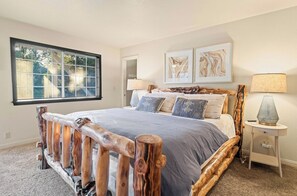 A bedroom with a wooden headboard, a large window, a bed with multiple pillows, two wall-mounted lamps, and framed artwork. - Private hot tub, Gorgeous views, Just minutes from the ski resorts & Lake (Big Bear Lake)