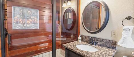 Un baño con cabina de ducha de madera, lavamanos sobre encimera de granito y un espejo grande.