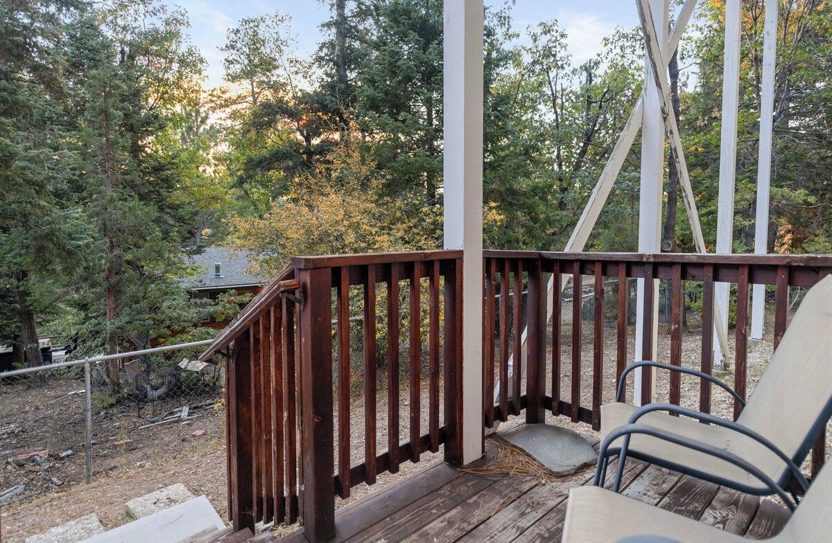 Una terraza de madera con barandilla de metal, una silla y vistas a zona boscosa.