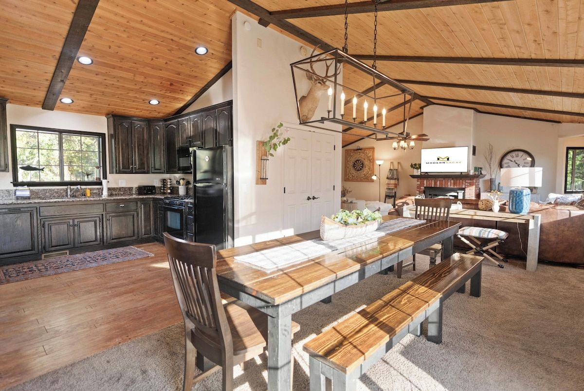 A spacious kitchen with dark cabinets, a large wooden dining table, and a hanging light fixture.