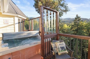 A hot tub on a deck with a wooden railing, a chair with a bear crossing pillow, and a sign indicating spa hours. - Private hot tub, Gorgeous views, Just minutes from the ski resorts & Lake (Big Bear Lake)
