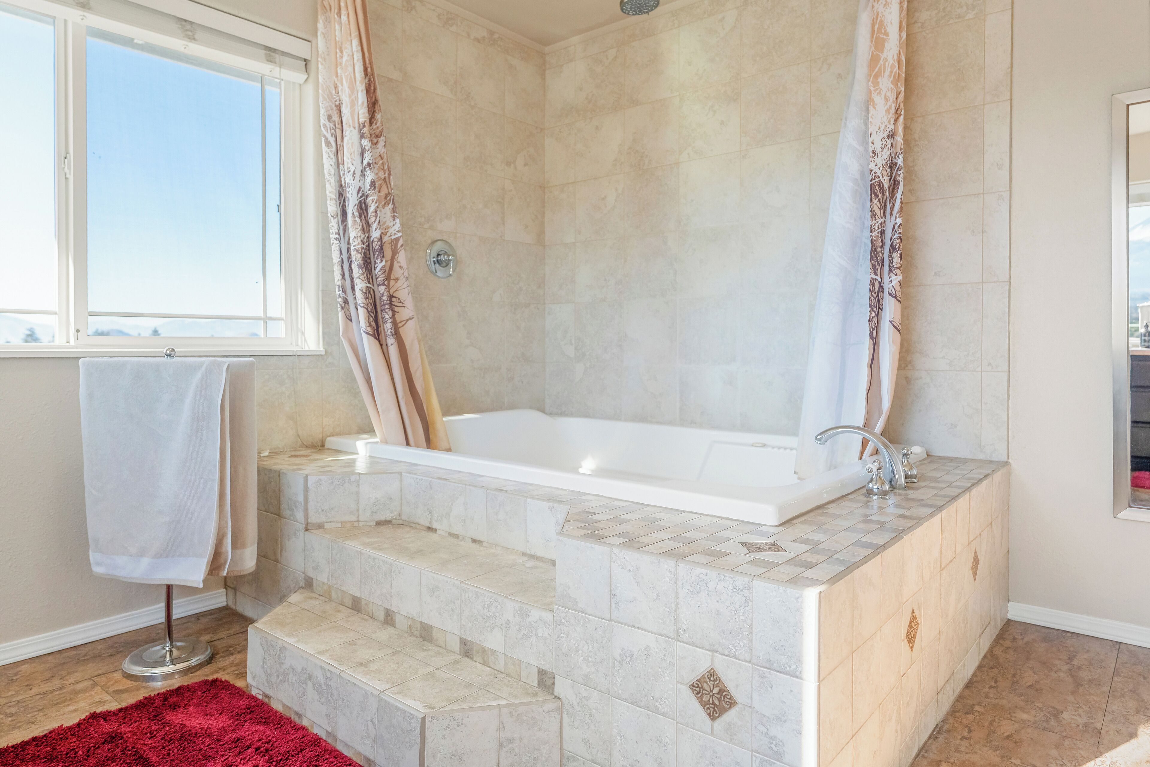 A bathroom with a large bathtub, a window, and a red rug.