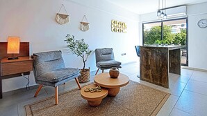Uma sala de estar moderna com dois poltronas cinzas, uma mesa de centro de madeira, uma pequena planta em vaso e um objeto decorativo na parede.