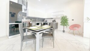 Une cuisine moderne avec des meubles blancs, une table à manger dressée pour quatre personnes et une plante en pot.