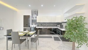 Une cuisine moderne avec des meubles blancs, un îlot central et un coin repas comprenant une table et des chaises en verre.