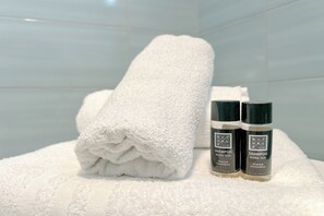 Ein ordentlich gefaltetes weißes Handtuch und zwei Shampooflaschen auf einer weißen Oberfläche.