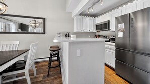 Eine moderne Küche mit weißen Schränken, einem Edelstahlkühlschrank und einer zentralen Kochinsel mit Barhocker.