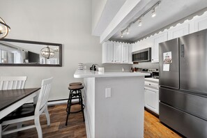 Une cuisine moderne avec des meubles blancs, un réfrigérateur en acier inoxydable et un îlot central doté de tabourets.