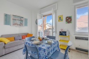 Ein Essbereich mit Esstisch für vier Personen, einer Couch mit Kissen, einem Fenster mit Aussicht und einer Wand mit Kunstwerken.
