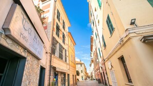 A narrow street with buildings on either side, a stone wall on the left, and a yellow building on the right. - Firpo - Apartment with Sea View, Loano, Italy (Loano)