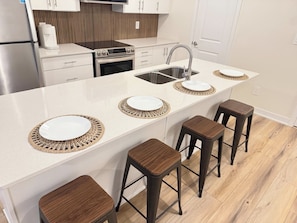 A modern kitchen with a central island, bar stools, a built-in oven, and a stainless steel sink. - Modern Townhome w Parking: 10 min to Boardwalk · Spa · Zoo (Pickering)