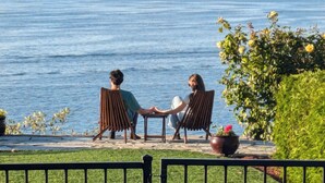 Twee personen zitten op stoelen met uitzicht op een waterpartij en verre bergen.