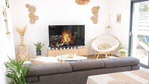 Una sala de estar moderna con un sofá gris, un televisor, una mesa de comedor y una lámpara de techo de mimbre.