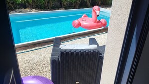 Vista de una piscina con un flotador con forma de flamenco rosa, rodeada de follaje y una silla de mimbre.