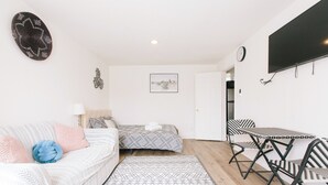 Et lille værelse med sofa, seng, spisebord med stole, fjernsyn og et ur på væggen.