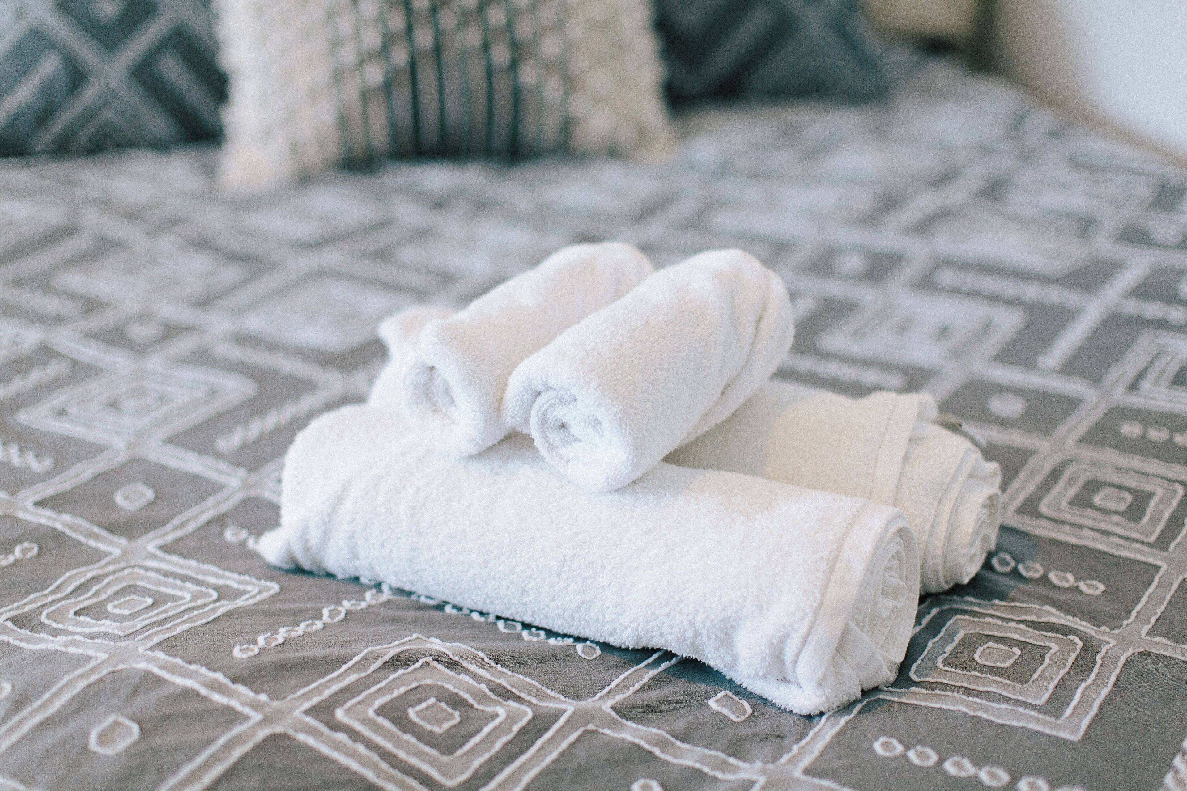 Uma cama com um cobreleito estampado e duas toalhas brancas enroladas.