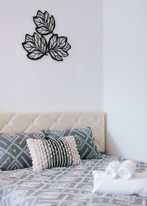 Une chambre à coucher bien aménagée, avec une tête de lit capitonnée, une literie à motifs, des coussins décoratifs et une œuvre d’art murale.