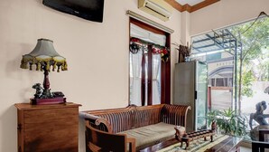 Ein Zimmer mit einer Holzsofa, einem Schrank, einem Tisch mit gemustertem Tischläufer und einem Fernseher an der Wand.