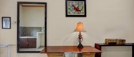 Un comedor con una mesa de madera, una silla de metal, una lámpara de pared, un cuadro enmarcado y un pequeño armario con libros.