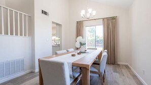 A dining room with a wooden table, white chairs, a chandelier, and a view of the outdoors through large windows. - Spacious 4-bedroom house in superb West Palmdale. Close to the mall. (Palmdale)