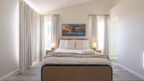 A modern hotel room with a large bed, two bedside tables with lamps, a painting on the wall, and a view of the outdoors. - Spacious 4-bedroom house in superb West Palmdale. Close to the mall. (Palmdale)
