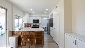 A modern kitchen with white cabinets, a central island with bar stools, stainless steel appliances, and a view to the outside. - Spacious 4-bedroom house in superb West Palmdale. Close to the mall. (Palmdale)