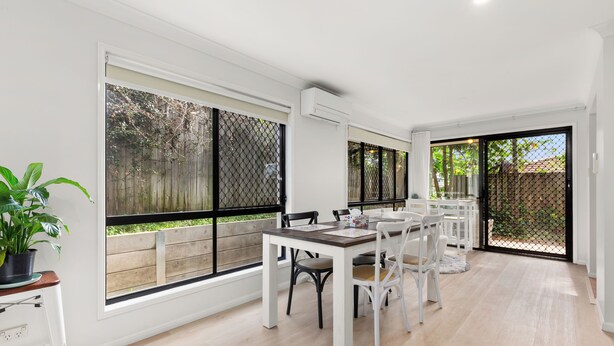 A spacious dining area with a long table and chairs, large windows with a view of a wooden fence, and an air conditioning unit mounted on the wall. - Stylish and comfortable 3-bedroom townhouse (Eight Mile Plains)