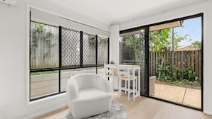 A modern room with a white armchair, a small table, and a large sliding glass door leading to a backyard. - Stylish and comfortable 3-bedroom townhouse (Eight Mile Plains)