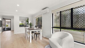 A spacious living area with a dining table and chairs, large windows with a view of the outdoors, and a modern white sofa. - Stylish and comfortable 3-bedroom townhouse (Eight Mile Plains)