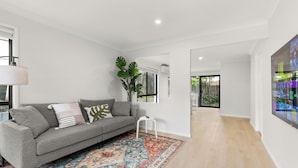 A modern living room with a grey sofa, patterned rug, and a large window with a view of greenery. - Stylish and comfortable 3-bedroom townhouse (Eight Mile Plains)