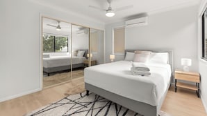 A modern bedroom with a large bed, a ceiling fan, a mirror, and a window. - Stylish and comfortable 3-bedroom townhouse (Eight Mile Plains)