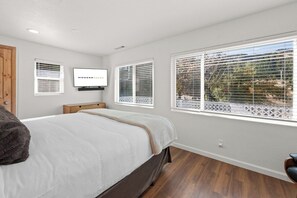 Ein Schlafzimmer mit einem Bett, einem an der Wand montierten Fernseher und drei Fenstern mit Jalousien.