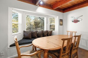 A dining area with a wooden table and chairs, a bench with cushions, and a window with blinds. - Mountain Retreat–Steps To Bear Mountain Ski (Big Bear Lake)