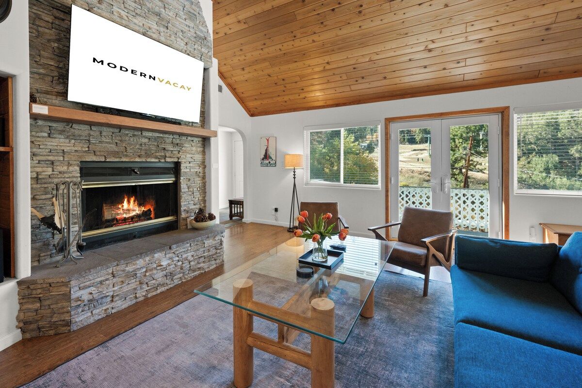 A modern living room with a stone fireplace, a glass coffee table, and a blue sofa.