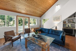 A modern living room with a glass coffee table, blue sofa, and wooden ceiling.